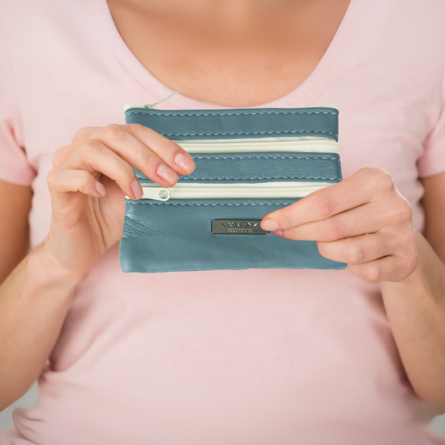 Hand holding a light blue leather coin purse with multi-zips, showing its small size and practicality