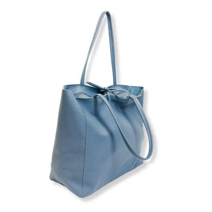 Angled three quarter view of denim blue full grain leather tote bag showing elegant design and depth.