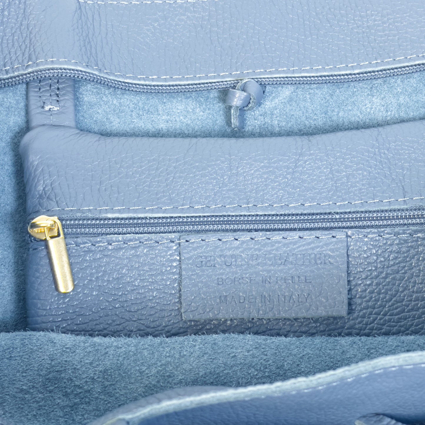 Close up interior detail of denim blue real leather tote showing gold tone zip and precise stitching.