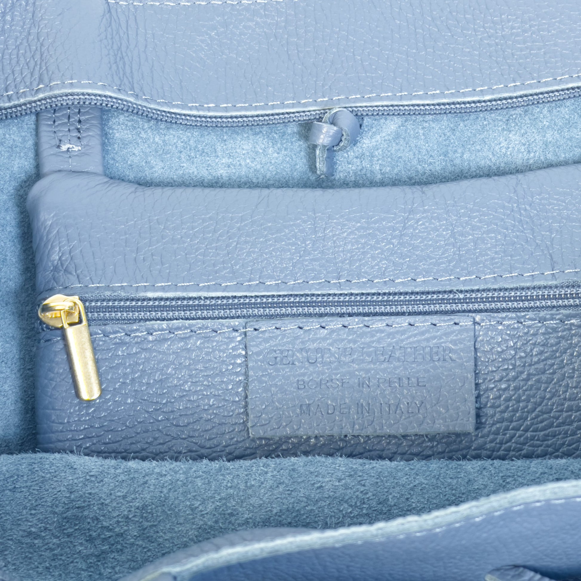 Close up interior detail of denim blue real leather tote showing gold tone zip and precise stitching.