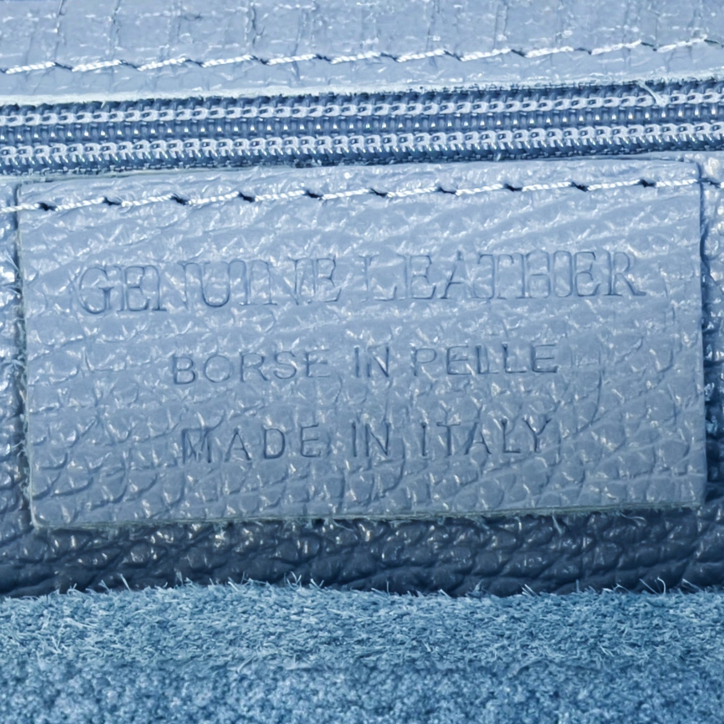 Close up detail of denim blue real leather tote bag showing texture contrast and gold tone zip.