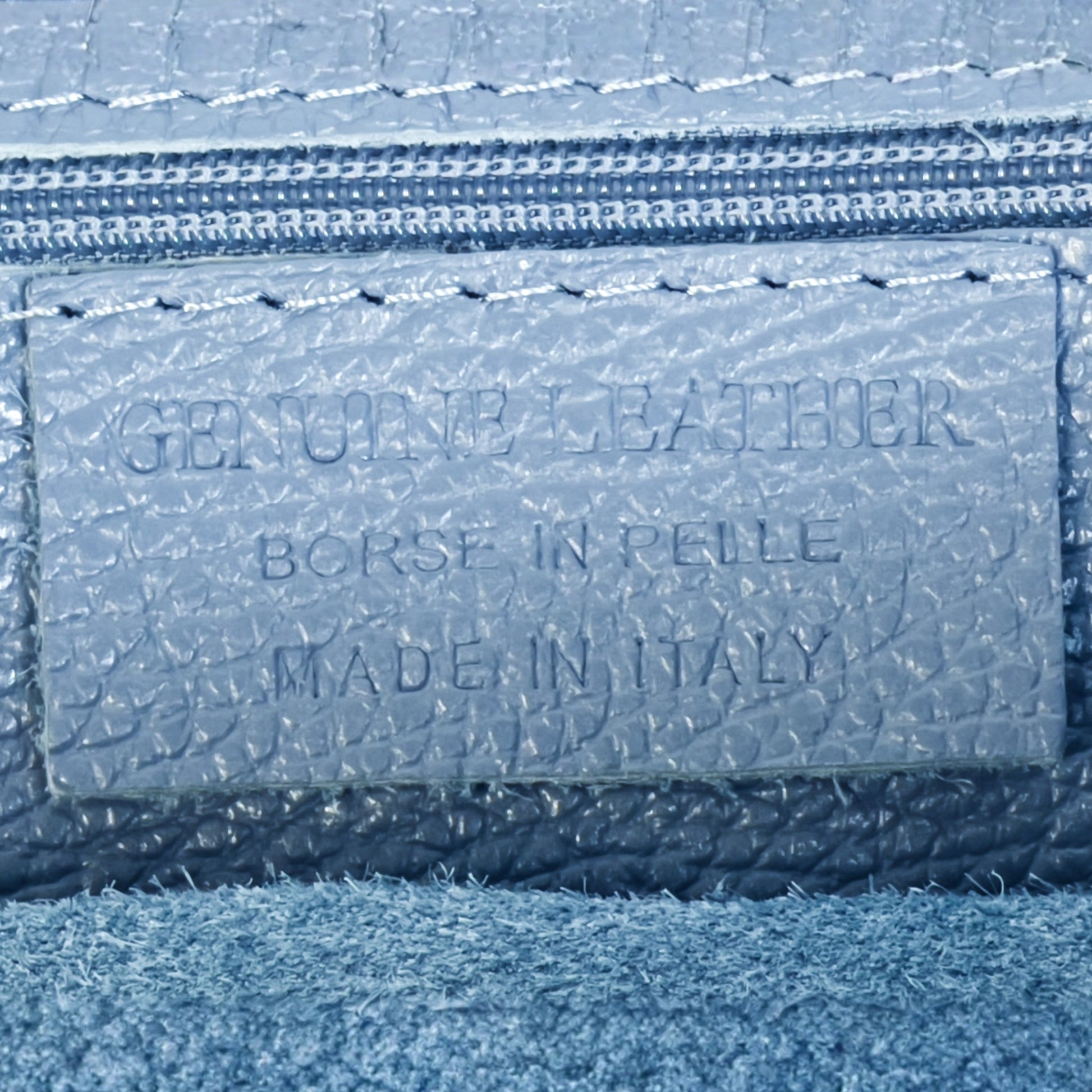 Close up detail of denim blue real leather tote bag showing texture contrast and gold tone zip.