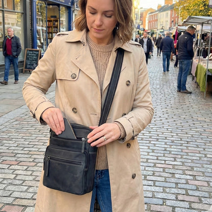 Woman wearing a black and grey hunter leather crossbody bag while standing outdoors in a casual outfit