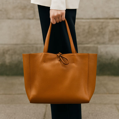 Dark-tan real leather tote bag, street scene holding bag with one hand.