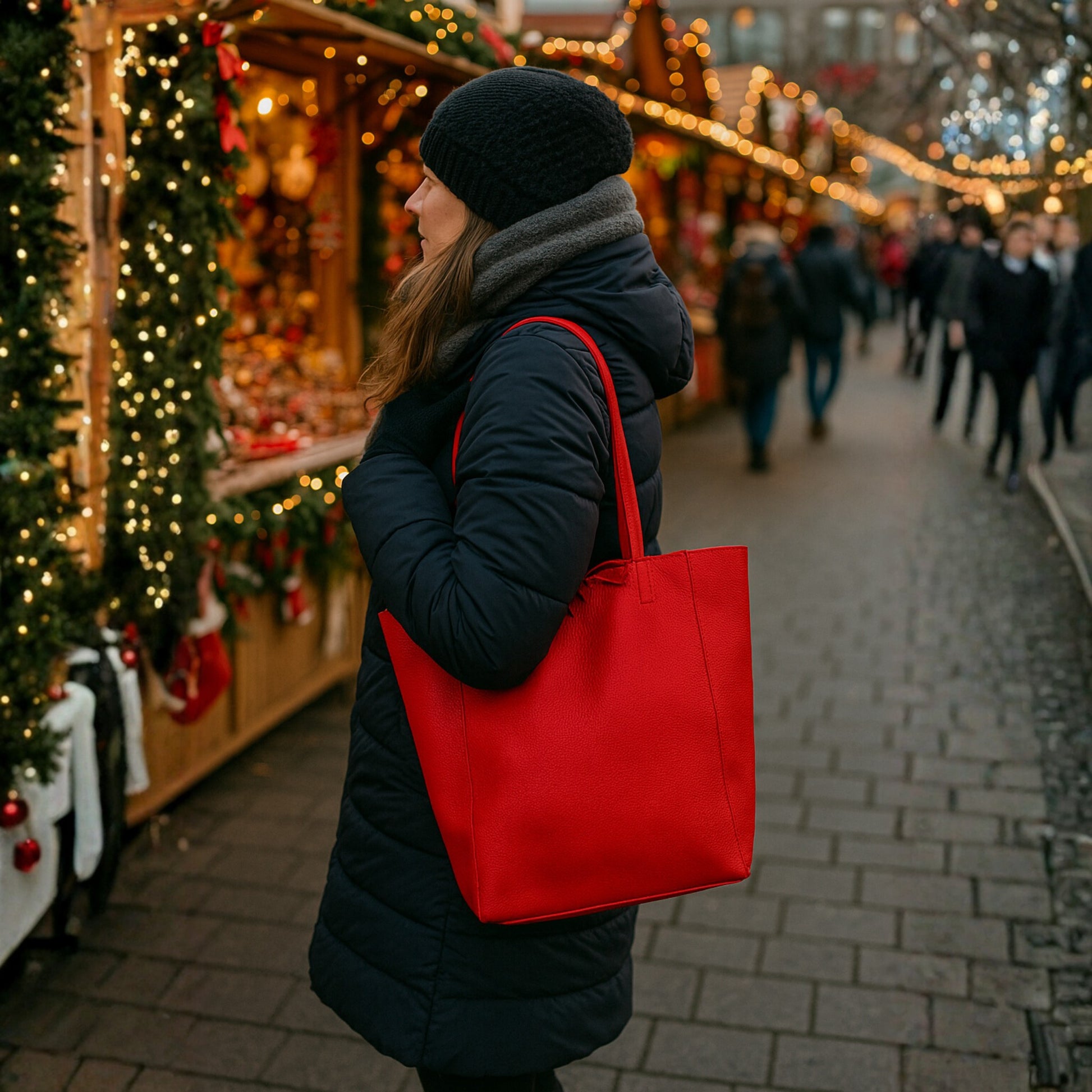 Lifestyle winter street view with a person holding a red real leather tote bag beside decorated market stalls.